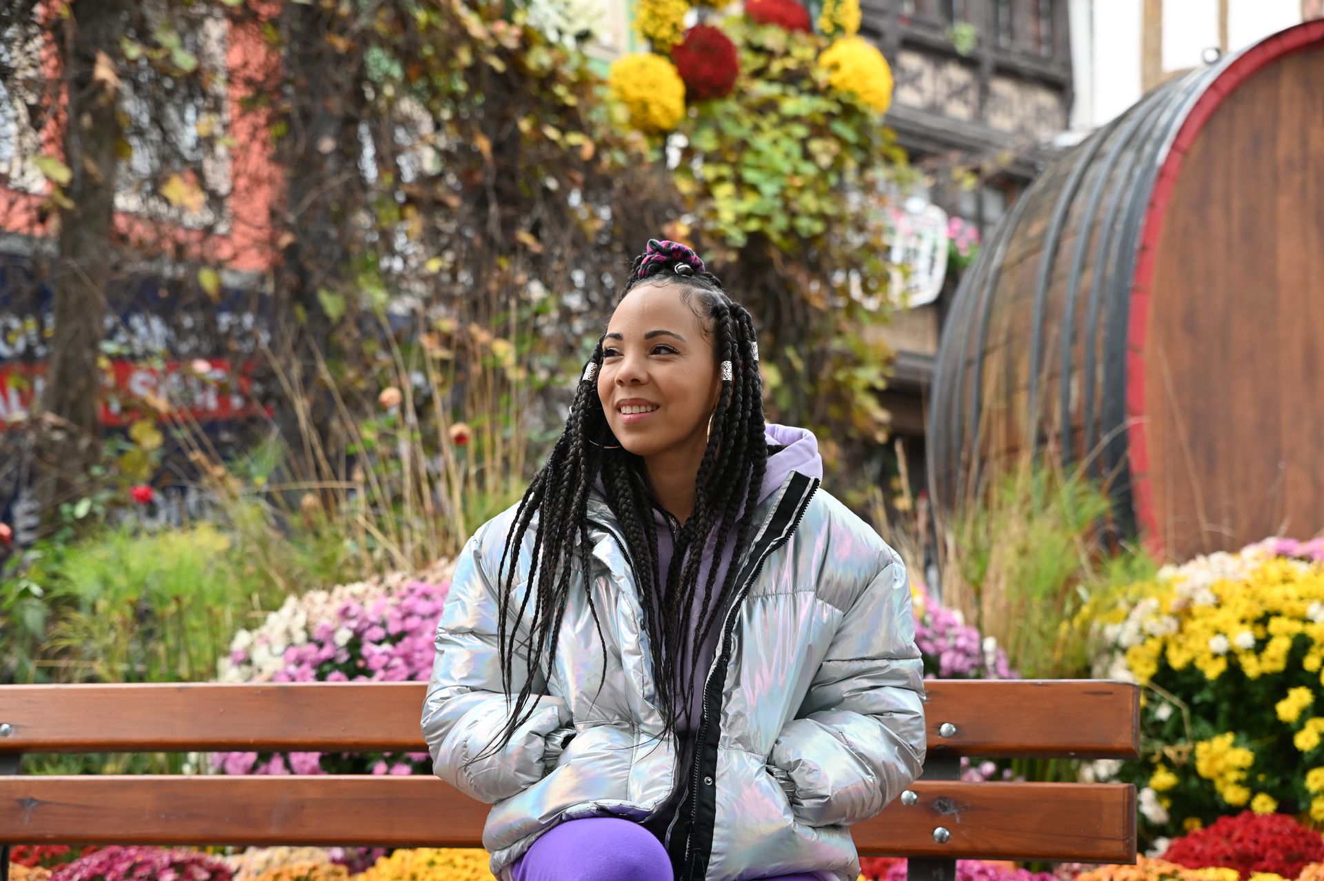 Une femme assise sur un banc devant un jardin fleuri, entourée de couleurs vives et de fleurs épanouies.